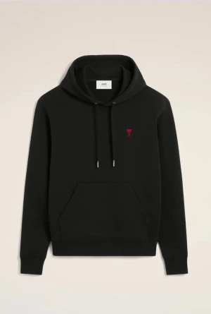 Svart hoodie från Ami med rött hjärta - Svart hoodie från Ami med klassisk huva och snörning. På bröstet finns ett litet rött hjärta som ger en snygg detalj. Tröjan har en stor magficka och ribbade muddar vid ärmslut och nederkant. Perfekt för dig som gillar stilrena och coola plagg.
