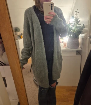 Grå stickad kofta med fickor - Mysig och lång grå stickad kofta med ribbad struktur och två praktiska fickor framtill. Koftan har en loose passform och långa ärmar, perfekt att slänga över en t-shirt för en chill look. Enkel och stilren design som funkar året runt.