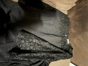 Svart klänning med spets från C&A - Svart klänning från C&A med snygga spetsdetaljer över axlar och ärmar. Klänningen har rund halsringning och ärmlös design med transparent spets upptill. Perfekt för dig som gillar en stilren look med lite extra edge.