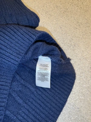 Marinblå stickad half zip från Polo Ralph Lauren - Säljer en marinblå stickad tröja från Polo Ralph Lauren med klassisk kabelstickning och röd broderad logga på bröstet. Tröjan har half zip, ribbad krage och muddar, samt långärmad passform. Materialet är 100% bomull och modellen är normal i passningen.