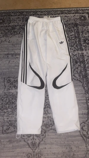 Adidas vita byxor  - Snabb leverans! 🚚 Dm för fler bilder! I fantastisk skick använd bara ett par gånger! Snygga vita träningsbyxor från Adidas med svarta ränder längs sidorna och Adidas-logga på höften. Byxorna har elastisk midja, meshfoder och coola svarta detaljer på benen. Perfekt för dig som gillar sportig stil och streetwear.