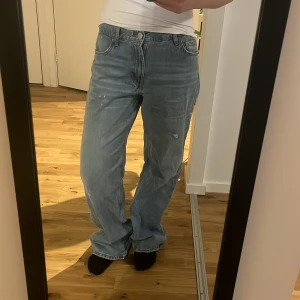 Ljusblå baggy jeans med slitningar - Säljer ett par ljusblå jeans med baggy passform och raka ben. Jeansen har klassiska fem fickor, knappgylf och coola slitningar framtill för en avslappnad vibe. 