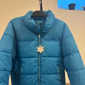 Blå pufferjacka med dragkedja - Blå pufferjacka från GINATRICOT med hög krage och silverfärgad dragkedja framtill. Jackan har två sidofickor med dragkedja och quiltad design. Perfekt för kalla dagar och har en modern, loose passform. Köpt för 699 lite fläckar vid händerna o vid fickorna 