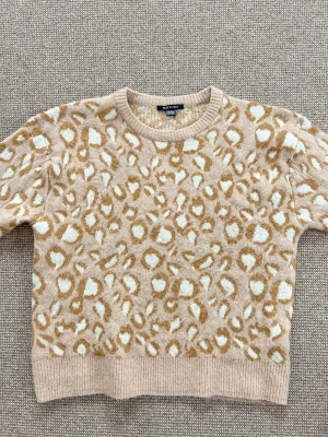 Beige leopardmönstrad stickad tröja Esmara - Säljer en beige stickad tröja från Esmara med leopardmönster i vitt och brunt. Tröjan har rund hals, ribbade muddar och långärmade ärmar. Perfekt för dig som gillar djurmönster och vill ha en mysig och trendig look.
