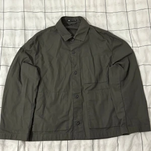 Grå overshirt från Zara, storlek M - Snygg grå overshirt från Zara med klassisk krage och knäppning framtill. Jackan har tre praktiska fickor på framsidan och raka, långa ärmar. Perfekt att slänga över en hoodie eller t-shirt för en chill look.