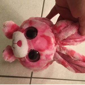 Rosa plysch handväska med nallehuvud - Supergullig handväska i mjuk plysch som ser ut som ett nallehuvud med stora svarta ögon och rosa glittriga öron. Väskan har ett handtag och är täckt av ett rosa och vitt mönster. Perfekt för dig som gillar söta accessoarer och vill sticka ut. Ny med etikett 