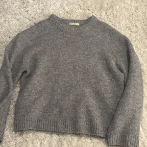 Grå stickad tröja från Gina Tricot - Mysig grå stickad tröja från Gina Tricot i storlek XS. Tröjan har rund halsringning, långa ärmar och ribbade muddar vid ärmslut och nederkant. Perfekt för kyliga dagar och enkel att matcha med jeans eller kjol.