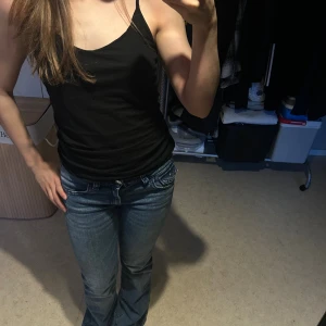 Blå bootcut jeans från Gina Tricot - Säljer ett par blå jeans från Gina Tricot med bootcut-modell och låg midja. Jeansen har snygga detaljerade bakfickor med knappar och broderi, klassisk femficksdesign och dragkedja. Har en liten defekt längst ner då dom har varit för långa för mig (161 cm).