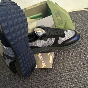 Valentino Garavani Rockrunner sneakers - Snygga Valentino Garavani Rockrunner sneakers i svart och grått med camouflagemönster. Skorna har snörning, platt sula med mönstrad undersida och detaljer i mocka och skinn. Perfekt för dig som gillar exklusiva och unika sneakers med streetkänsla.