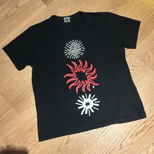 Svart Comme des Garçons t-shirt XXL - Svart t-shirt från Comme des Garçons BLACK i bomull, med coolt grafiskt tryck i vitt och rött. Köpt i Asien så storleken är inte så stor, passar som en L. Använd ytterst få gånger.