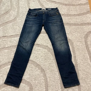 Replay Anbass Hyperflex jeans blå - Snygga Replay Anbass Hyperflex jeans i mörkblå tvätt med lätt slitningar och klassiska fem fickor. Slim passform och stretchigt material för extra komfort. Coola detaljer med kontrastsömmar och Replay-läderpatch bak i midjan.
