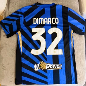 Inter Milan Dimarco #32 Nike matchtröja - Snygg Inter Milan fotbollströja med Dimarco och nummer 32 på ryggen. Tröjan är blå och svart med randigt mönster, guldiga detaljer och klubbmärke på bröstet. Tillverkad i lätt polyester, har korta ärmar och V-ringad krage. Perfekt för dig som älskar Serie A och vill ha en autentisk supportertröja.