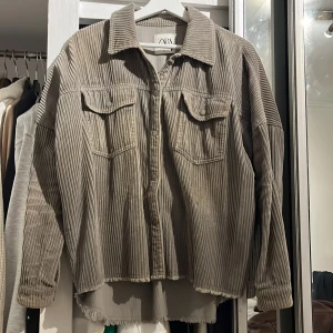 Grön overshirt i manchester från Zara - Säljer en grön overshirt från Zara i mjuk manchester med snygga vertikala ränder. Modellen är loose fit med långa ärmar, två bröstfickor med knappar och rå kant nedtill för en cool vibe. Perfekt att slänga över en t-shirt för en chill look. 