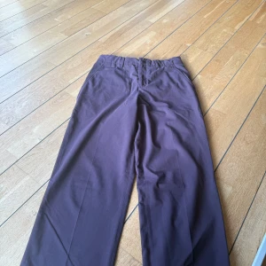 Mörklila kostymbyxor med raka ben - Snygga mörklila kostymbyxor med raka ben och klassisk passform. Byxorna har hällor för bälte, diskreta bakfickor och stängs med dragkedja och knapp framtill. Perfekta för en clean och stilren look.