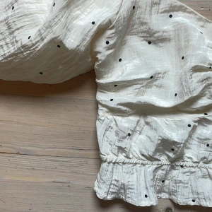 Vit prickig blus med puffärmar - Supersöt vit blus med svarta prickar och stora puffärmar från Gina tricot i storlek S. Toppen är croppad med volangkant nertill och smockad rygg för extra komfort. Gjord i ett lätt, krinklat tyg som ger en cool struktur. Perfekt för dig som gillar romantisk och trendig stil. Jag har använt denna endast en gång och blusen är därför i toppskick (nästintill nyskick)! Skulle gärna använt den mer då den är så fin men det är inte en tröja gjord för mig helt enkelt. 