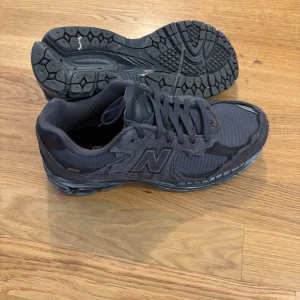 Mörkgrå New Balance 2002R sneakers - Säljer ett par mörkgrå New Balance 2002R sneakers med mesh och mocka-paneler. Skorna har en chunky sula, snörning och den klassiska N-loggan på sidan. Perfekta för dig som gillar streetwear och vill ha en bekväm och snygg sneaker till vardags.