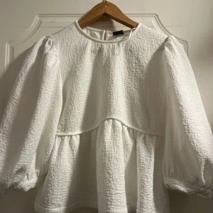 Vit strukturerad blus med puffärm - Säljer en vit blus med strukturerat tyg och voluminösa puffärmar. Blusen har rund halsringning och en lös, flowy passform med markerad söm under bysten. Perfekt för dig som gillar en romantisk och trendig look.