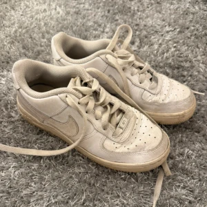 Nike Air Force 1 vita sneakers - Klassiska Nike Air Force 1 sneakers i helvitt skinn med perforerad tå och snörning. Snygg och tidlös modell med rund tå och platt sula, perfekt för dig som gillar streetstyle. Diskret Nike-logga på sidan och AF1-detalj på snörningen.Smutsiga men går bort om man tvättar.