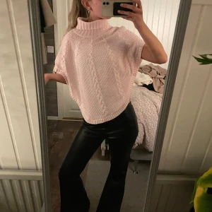 Stickad poncho - Säljer en ljusrosa stickad polotröja med korta ärmar och snygga kabelstickade detaljer. Tröjan har en hög krage och är loose i passformen, vilket gör den superbekväm och chill. Perfekt att slänga på sig när det är lite kyligt ute. Finns ingen kappa men skulle säga xs!