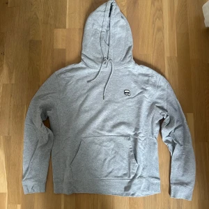 Karl Lagerfeld hoodie - Snygg grå hoodie från Karl Lagerfeld med liten logga på bröstet och diskret tryck bak. Tröjan har huva med snörning, stor magficka och långa ärmar. Perfekt för chill dagar och streetstyle. Mjuk bomullskvalitet som känns skön mot huden.