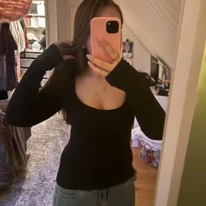 Svart långärmad topp från Bik Bok - Svart långärmad topp från Bik Bok i storlek S. Modellen är figurnära med djup rundad halsringning och stretchigt material som sitter snyggt på kroppen. Perfekt att styla med jeans eller kjol för en clean look. Det finns ett litet hål vid lappen, men som ej syns när tröjan är på(se sista bilden). 