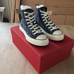 Valentino Garavani höga sneakers blå - Snygga höga sneakers från Valentino Garavani i blått denimtyg med mönster och vita detaljer. Skorna har vit gummisula, rund tå och klassisk snörning. Logga på plösen och undersidan. Kommer med extra skosnören och dustbag. Fick dessa i konfirmation present men passar mig inte i smaken. Dessa köptes i Tyskland i en butik av massor av olika märkes plagg och accessoarer där vi köpte dem för 760 euro 