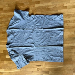 Grå t-shirt från Polo Ralph Lauren - Snygg grå t-shirt från Polo Ralph Lauren med klassisk passform och rund hals. T-shirten har en liten grön broderad logga på bröstet och är tillverkad i mjuk bomull. Perfekt för en avslappnad och stilren look.