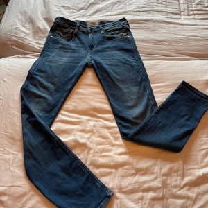 Blå Replay Anbass Hyperflex jeans - Snygga blå jeans från Replay, modell Anbass Hyperflex. Jeansen har klassisk femficksdesign, normal passform och raka ben. Tillverkade i stretchigt jeansmaterial för extra komfort. Märkesdetaljer på fickor och midjeband. Perfekta för en avslappnad och trendig look.