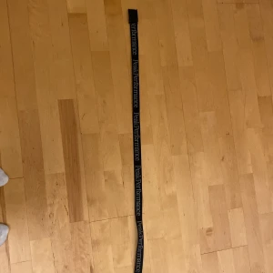 Svart Peak Performance bälte - Snyggt svart bälte från Peak Performance med tydlig logotyp längs hela bandet. Bältet har en robust metallspänne med graverad logga och är gjort i slitstark polyester. Perfekt för dig som gillar sportig och clean stil.