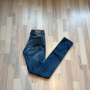  Nudie Jeans 28/34 - Snygga blå jeans från Nudie Jeans med klassisk orange söm och smal passform. Jeansen har fem fickor, normal midja och raka ben som smalnar av. Tillverkade i mjukt denimtyg som sitter skönt hela dagen.