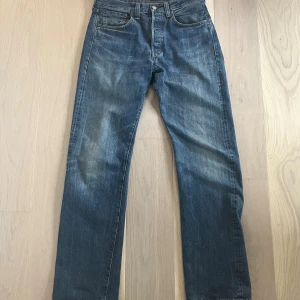 Levi's 501xx ”Big E” selvage jeans - Klassiska Levi's 501xx jeans i mörkblå tvätt med raka ben och hög midja. Jeansen har fem fickor, knappgylf och snyggt sliten, rå kant längst ner på benen. Tillverkade i robust bomullsdenim med selvedge-detalj på insidan av benslutet.