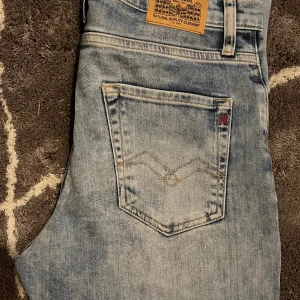Ljusblå Replay jeans slim fit  - Säljer ett par ljusblå jeans från Replay med klassisk femficksdesign, snygga detaljer på bakfickorna och läderpatch i midjan. Jeansen har rak passform och dragkedja i gylfen. Perfekta för dig som gillar en avslappnad stil.