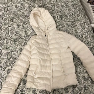 Vit pufferjacka från FB Sister XS - Säljer en snygg vit pufferjacka från FB Sister i storlek XS. Jackan har huva med snörning, dragkedja framtill och två fickor med dragkedja. Perfekt för kalla dagar när du vill hålla dig varm och se fräsch ut.