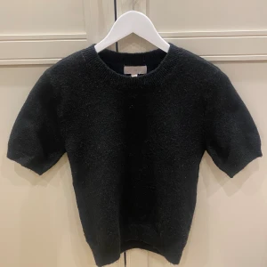 Svart stickad tröja från H&M - En svart stickad tröja från H&M i storlek XS. Tröjan har korta ärmar, rund halsringning och en klassisk, enkel design. Perfekt för lager-på-lager och funkar året runt. Mjuk och skön känsla tack vare det stickade materialet.