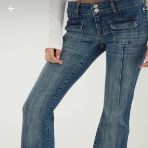 Blå bootcut jeans med fickdetaljer - Snygga blå jeans med bootcut passform och dubbla framfickor med lock. Jeansen har låg midja och markerade sömmar längs benen för en cool look.