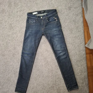Replay Anbass slim fit jeans blå - Nypris 1800 kr.  Snygga Replay Anbass jeans i mörkblå tvätt med slim fit passform, kontrastsömmar och läderpatch bak. Jeansen har en smal siluett och är tillverkade i stretchigt denim för skön komfort. Perfekt för dig som gillar stilrena och moderna jeans.