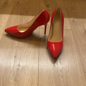 Röda pumps med spetsig tå och klack - Snygga röda pumps med hög klack och spetsig tå. Skorna har en glansig finish och är tillverkade i syntetmaterial. Perfekt för dig som vill sticka ut med en färgstark och elegant look. Insidan är beige och sulan är platt framtill.