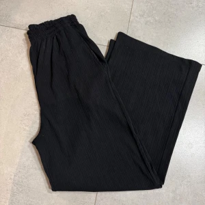 Svarta vida byxor med resårmidja - Svarta byxor med diskret ribbad struktur och breda, raka ben. De har elastisk midja för extra komfort och praktiska sidfickor. Perfekta för en chill och avslappnad stil. * Fint skick - använd 1 gång * Skickar samma dag eller dagen efter  *  Rökfritt hem * Passa på att kolla mina andra annonser, du får mängdrabatt och jag tackar ja till rimliga bud  * 🤍