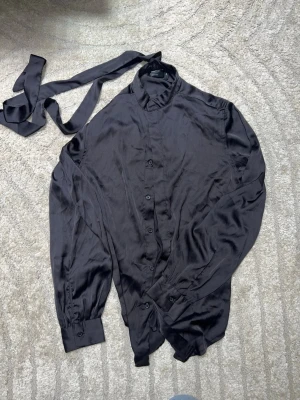 Svart satin skjorta med knyt från ASOS - Svart skjorta i satin från ASOS DESIGN med knytband i halsen. 2xs men större i passform som small