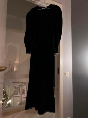 Svart lång stickad klänning från Adoore - Supersnygg svart långklänning från Adoore med ribbad stickad struktur. Klänningen har långärmade ärmar och vit snörningsdetalj vid ärmslut och nederkant. Rundad halsringning och figurnära passform som framhäver siluetten. Klänningen är nästintill oanvänd och i väldigt fint skick! Säljer för 1100 kr (köpte för 1795 kr)
