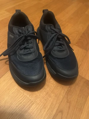 Mörkblåa Hugo Boss skor - Snygga mörkblåa sneakers från BOSS med mesh och skinnpaneler, rund tå och platt sula. Skorna har snörning och coola prickdetaljer på hälen. Perfekta för dig som gillar stilrena och sportiga vibes.