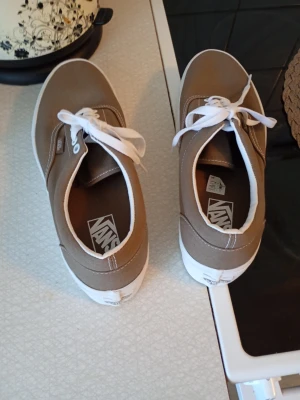 Beige Vans sneakers med vit sula - Säljer ett par stilrena Vans sneakers i beige med vit sula och vita snören. Skorna har rund tå och är tillverkade i canvasmaterial med klassisk Vans-logga på insidan. Perfekt för dig som gillar enkel och clean streetstil.
