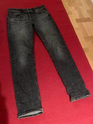 Jeans - Säljer ett par mörkgråa tapered jeans från Jack & Jones med snygga slitningar. Rak passform hela vägen ner. Strlk 32/34