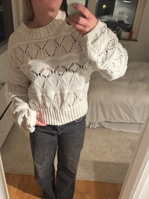 Vit stickad tröja med mönster - Säljer en vit stickad tröja med snyggt hålmönster och bred ribbad kant vid hals, ärmslut och nederkant. Tröjan har långärmade och loose passform, perfekt att styla med jeans eller kjol. Den har en cool och avslappnad vibe som passar till många olika looks.