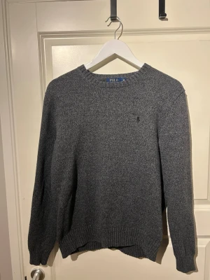 Grå stickad tröja från Polo Ralph Lauren - Säljer en mörkgrå stickad tröja från Polo Ralph Lauren i storlek M. Skicket är 8/10 och används 1 gång utav mig.  Nypris 1400