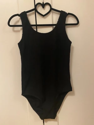 Svart ribbad baddräkt 158/164 - Säljer en svart ribbad baddräkt för barn i storlekarna 158/164. Baddräkten har breda axelband och rundad halsringning.💕