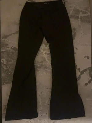 Svarta bootcut kostymbyxor - Snygga svarta kostymbyxor från bikbok i gamla Vera modellen med bootcut-snitt och klassisk design. Byxorna har låg midja och är tillverkade i ett slätt tyg som ger en stilren look. Har slut längst ner vid benen. Är i petit längd så passar dig som är runt 160cm. Perfekta för dig som gillar en tidlös och trendig siluett.