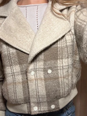 Rutig teddyjacka från Pull&Bear - Supermysig teddyjacka i beige och bruna toner från Pull&Bear. Jackan har rutigt mönster, bred krage och knappar framtill. Den är croppad med ribbade muddar vid ärmslut och midja. 