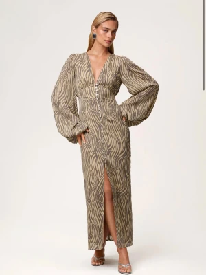 Zebramönstrad långklänning från Adoore - Supersnygg långklänning från Adoore med zebramönster i beige och brunt. Klänningen har v-ringning, långa puffärmar och knappar framtill samt en slits. Materialet är lätt och ger en lyxig känsla. Perfekt för dig som vill sticka ut med stil. Den är helt ny med prislapp, storlek 42/XL