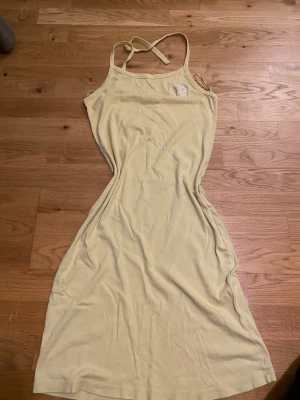 Ljusgul långklänning med broderad blomma - Säljer en ljusgul halterklänning med smala axelband och en broderad blomdetalj på bröstet. Klänningen har en enkel passform är tillverkad i mjukt bomullsmaterial. Perfekt för varma dagar och snygg med bikini under! 